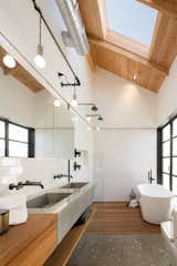 A skylight illuminates the neutral palette of this master bathroom, letting bathers peacefully contemplate the clouds from the privacy of its enclosed walls. The wood counter, concrete sink, and pebbled floor create a calming, textured space, and the natural materials stand out against the white subway tile.