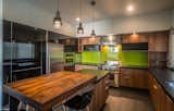 A green backsplash adds a dash of color while the kitchen island sits under a series of pendant lights. The kitchen features Electrolux and Wolf appliances.