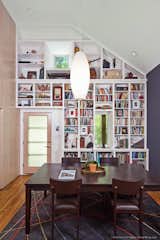 The front door opens onto a combination dining/library, with a vaulted ceiling. The entry wall features a floor-to-ceiling custom bookcase with a window set high to capture light and a view of the ash tree in the yard. Whitewashed maple plywood strips in a vertical running bond pattern act as a warm “tile” and are the sole decorative flourish for the adjacent wall. Photo by Patrick Wong.