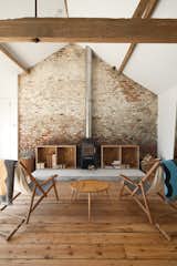 Subverting the traditional, conservatively cozy British barn conversion, Carl Turner created a getaway in rural Norfolk for himself and his friends to visit, repose, and consider the beauty of agrarian minimalism. In the converted barn, a modern fireplace with a sleek, shiny chimney contrasts with the wide, reclaimed wood floorboards and textured exposed brick wall.