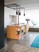 By using color, wood, and polished concrete floors, this apartment in Berlin is full of personality. In the kitchen, polished statuario marble covers both the island's countertop and the backsplash in the custom kitchen cabinet block. PSLAB designed the light fixtures, and the island has open shelving incorporated into it for easy access to cookbooks and other reading material.
