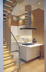 By sharing a ceiling, the kitchen and the staircase are intertwined. The staircase contains a built-in refrigerator and storage. The staircase features white oak wood while the kitchen island stands out with white painted millwork and geometric tile.