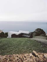Initially unassuming, the E/C home appears hidden from the road, perched on the sloping edge of the island and partially wrapped in the basalt walls from an 18th-century farmhouse. Architects Ines Vieira da Silva and and Miguel Vieira approached the site with a vision to create a relationship with the landscape; they designed the 2,600-square-foot holiday home to not only be a simple escape, but also to frame the weathered coast and reflect its past. “Both paths to the house were designed with basalt stone, as if they were still a rural path,” Vieira da Silva says.
