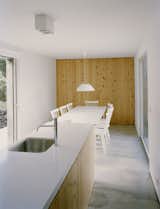 Kitchen, Concrete Floor, and Pendant Lighting The quiet, minimalist kitchen features a wall in the same “criptoméria" wood used for the bookshelf in the living room. A Davide Groppi Punto 2 PL light hangs over the dining table.  Search “Jambox-holiday-guide.html” from This Modern Coastal Escape Sits Within 18th-Century Stone Walls
