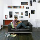 Mathieu Vinciguerra reads in front of the distinctive storyboard shelves in his Paris apartment, which H20 Architects designed to accommodate a portion of his massive comic book collection. “We wanted to feature the comics without letting them become visually overwhelming,” says Antoine Santiard of H20. “So we developed this box concept, where bits of white space separate all the shelves.” Photo by Céline Clanet.  Photo 4 of 6 in Library Style: 6 Looks at Books in the Modern World by William Lamb