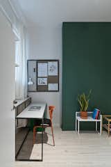 One student bedroom features the second green accent wall. Each bedroom is about 140 square feet and includes places for sleeping and studying, plus built-in IKEA wardrobes. The custom desk is paired with an orange IKEA chair. The small metal accent table and magnetic wall board are also by Wierciński.