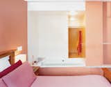 Bedroom, Wall Lighting, Night Stands, Storage, and Bed A bedroom in a renovated townhouse in Harlem, New York, makes the most of a tight space with orange-tinted pink walls. Pink bedding keeps the space monochromatic but adds depth with a range of reddish tones.  Search “toy glass vase pink green” from Harlem Renaissance