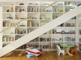 With glass raillings, the stairs to the second level invite glimpses through to a double-height bookshelf, filled with books and collected artifacts. Every room in the house is designed with the children in mind, and contains a dedicated space for them—for instance, the craft table under the stairs.