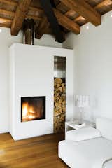 At a renovated farmhouse in the Italian countryside, a crisp, modern white plaster fireplace and hearth infuse the interior with coziness and warmth.