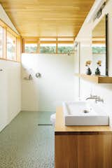 In the bathroom, a thin pane of glass separates the shower; an Aquaplane sink by Lacava hovers above 

a built-in vanity illuminated by a lean Adelphi light by Oxygen Lighting; and blue-green glass penny tiles by Terra Verre decorate the floor. The absence of a door, combined with windows on two sides, makes the bathroom feel like a continuation of the overall space.