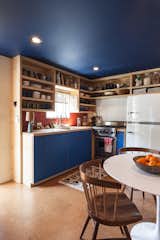The kitchen cabinetry echoes the new blue ceiling. The brick tile is from Heath Ceramics, as is the dinnerware. Behind the Viking stove is powder-coated corrugated metal ("Very trailer," says the designer). The refrigerator is from Big Chill. On the table is a bowl by Victoria Morris.