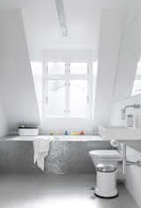 Bath Room, Drop In Tub, and Wall Mount Sink Sofie and Frank built a box around an ordinary glass fiber shell bathtub, then covered it in a mosaic of shower tiles. Natural light from a large dormer window gives the tiles an almost iridescent glow. The toilet is Duravit.  Search “copenhagen elevations achitectural print maple frame” from Black, White, and Gray All Over: Monochromatic Copenhagen Townhouse