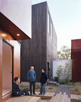 Schenk, Kim, and Kaewlai chat outside of X-Small, standing on the reclaimed wood used to build the boardwalks that connect all four properties. The translucent corridor connecting Small and Medium illuminates the common space throughout the evening.  Photo 8 of 11 in Four Houses and a Future