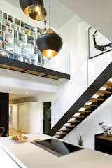 The couple’s white Bulthaup kitchen is set within a double-height volume hung with Tom Dixon Beat lights, arranged in a custom configuration by interior designer Maria Rosa Di Ioia. Overhead, Cubit shelving artfully displays books and objects, accessible by a glass-walled footbridge added during the renovation.