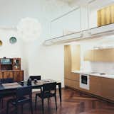 The kitchen fits neatly on one wall. The architect reads at a black Ligne Roset dining set, beneath a Col pendant lamp by Francisco Luján. The tublar steel mezzanine rails were designed by Mikulionis, who enjoyed being exempt from the safety concerns that a client would force on him.