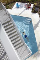 Exterior concrete staircases cantilever over the pool and provide circulation between interior and exterior living spaces. Perforated metal railings provide a protective enclosure while creating patterns of light that mark the movement of the sun. The recycled plastic chairs are by Loll.
