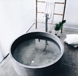 A freestanding, circular concrete tub sits beside a bamboo towel rack in this photo shared by @thebeachpeople.