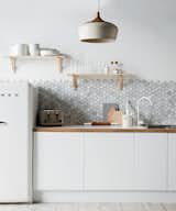 A backsplash of hexagonal Carrara marble from Australia's Di Lorenzo Tile offsets the minimalist white cabinetry and countertops in this kitchen styled by Jackie Brown. 