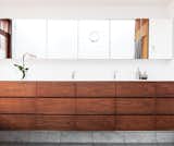 Architect Paul Syme designed custom storage units with dark-stained walnut fronts that provide a place for everything in his clients’ Toronto bathroom. The wall-to-wall mirror and the Corian counter are custom, and the faucets are by Vola.