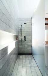 The standing shower is set off by etched-glass panels supported by stainless-steel hardware. There is no threshold; instead, the tile within the shower zone slopes down very slightly to a floor trough with a custom stainless-steel grille. Along the wall, a Corian shelf—“the longest soap dish in the world,” resident Don Evans jokes—runs the length of the space.