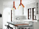 Barbara Hill had the overhead lighting in the kitchen customized by Rich Brilliant Willing in a pert orange that accents the primarily black-and-white interior scheme. She added a stainless steel kitchen island by Bulthaup, its glossiness and "clean feel" tempered by the plastic stacking stools designed by Konstantin Grcic for Magis. The cabinets, appliances, countertops, and marble tile were kept as-is, with the addition of several coats of white paint in order to blend seamlessly with the walls.