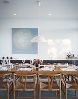 A pendant lamp by Hans Wegner for Carl Hansen & Søn hangs above a custom dining table by Cabinet. The paint is Cloud White by Benjamin Moore, and the painting, titled Meshed, is by Anna Yuschuk.