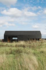 Exterior, Barn Building Type, and Wood Siding Material "It only cost about $48,000 to build, which was incredibly cheap," says Turner of the Stealth Barn. "We got the Timber Frame Company to supply the shell, then we clad it and fitted out the interior and windows ourselves. The idea was to take the archetypal black tar-painted agricultural building and make an almost childlike icon of that."  Photos from A Pair of English Barns Hide Unabashedly Bold and Budget-Friendly Minimalist Interiors