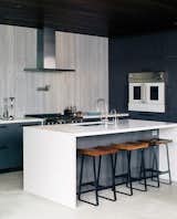 In this sleek kitchen, the range and wall oven are by BlueStar, the hood is from Zephyr, and the island is Caesarstone.