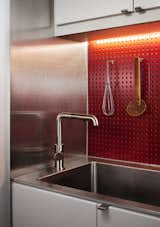 A Boston loft in a former textile factory receives a minimal, efficient kitchen at the hands of Bunker Workshop. The client wanted to be able to prepare meals efficiently, so a red steel pegboard backsplash lets him easily access cooking utensils. The cabinets are IKEA.