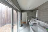 The bathroom features floor-to-ceiling glass walls and louvered windows to help the narrow space feel larger.