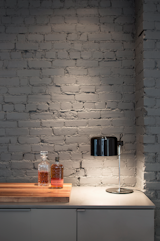 The kitchen’s exposed brick wall matches its cabinetry in Benjamin Moore’s “Kendall Charcoal” hue. A Joe Colombo Coupé 2202 table lamp by Oluce illuminates a walnut cutting board.