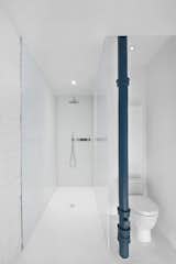 The cast pipe is original to the property and stands next to a Starck 3 toilet by Duravit. A glossy white epoxy floor and a glass shower adhere to the interior's minimal aesthetic.