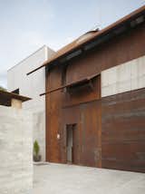 In Sitges, Spain, Olson Kunding crafted a live-work house for two artists. Large panels of steel arch from the ground over the entrance, curving to create part of the building’s roof. Materials with a strong industrial aesthetic, including untreated steel and cast-in-place concrete, are used in the entry sequence, while the rear of the building opens to the landscape. Photo by: Nikolas Koenig.