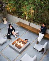 In a Manhattan Beach home, homeowner Matt Jacobson and architect Michael Lee designed the long steel-and-Ipe bench surrounding a square, concrete outdoor fire pit, which suspends from the low concrete wall in their outdoor space. Dukes relaxes on a Willy Guhl Loop chair with her German Shepherd, Major.