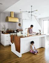 The Mandayam–Vohra family's Brooklyn kitchen is highlighted by a gold hood that complements Workstead’s signature three-arm chandelier, shown here in its horizontal configuration.