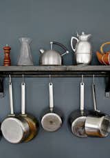 Small kettles and metal pots rest and hang on a wooden shelf in the kitchen.