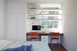 The guest bedroom also doubles as the primary homework area for the kids. Orange school chairs add a playful pop of color to the space. Large window openings bring in light and offer views of the lush surroundings.