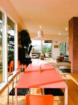 The naturally-lit dining room features a long red-orange table and metal-and-wicker chairs.