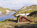 Tucked away on the edge of a small lake surrounded by mountains and topped off with a grass-covered roof, this hunting cabin designed by Snøhetta is made with locally sourced stones. The 376-square-foot prefab mountain hut sleeps up to 21 guests around a central fireplace.