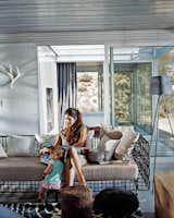 Taalman sits with their daughter, Oleana, in the living room on a metal lounge designed by Kenneth Cobonpue. Glass walls emphasize views and greatly expand the sense of space in the 1,100-square-foot house. Through the glass wall behind her is the fire court and behind that the master bedroom.