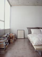 Bedroom, Bed, and Concrete Floor Who needs shelves when there's plenty of floor space? Stacks of books and a framed print sit alongside a Peter Maly Ligne Roset bed, reupholstered in stiff linen.  Photo 8 of 11 in Stripped Ease