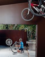 Pierre Kozely mends his bike on a patio in the rear yard, seen from their garage—which was transformed into a media room. Behind him is a Cor-Ten rolling gate that gives access 

to the back alley.