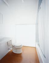 Upstairs, simple porcelain pieces such as a Kohler toilet adorn the modest master 

bathroom. Beneath the downward-pitched ceiling, a polycarbonate-panel wall brings in light from the south-facing skylight behind.  Photo 9 of 11 in New Beginnings