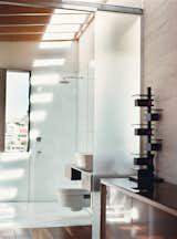 The sun cuts down into the upstairs bathroom through skylights, casting rhythmic shadows of roof beams onto the floor and walls. The bathroom includes a cantilevered toilet by Catalano.
