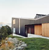 The home is mostly clad in black trapezoidal-profile steel, with cedar boards lining what the owners call the “human spaces”—external passages between buildings. A solar hot water system perches on the roof.