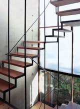 The wood-and-steel open staircase wends its way up three stories, supported by a concrete structural wall embedded with PVC tubes and bare lightbulbs.