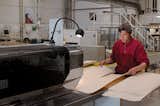 A worker runs two strips of veneer through a machine that glues the edges together.