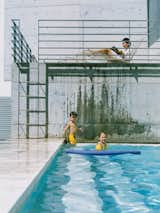 The kids and their mother relax in the pool area, their figures framed against a monochromatic background of steel and concrete.