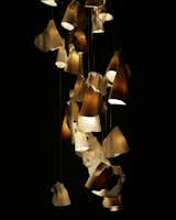 "The 21 was inspired by the sporadic and often discordant arrangements that barnacles form on a rock surface," says Omer Arbel. "Each pendant is made of thin sheets of raw white porcelain wrapped around frosted blown borosilicate glass cones of varying sizes. The result is a gentle contrast between diffused light passing through the translucent white porcelain skin and sharp, crisp light passing through the frosted Borosilicate glass trumpet shape on the interior of the pendant. Traditionally, porcelain is cast or sculpted into very specific forms. Our goal for the 21 Series was to design a process which yields different forms in every iteration. We let the material bend and fold according to its own intrinsic logic so every piece is completely unique."