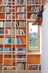 To make the most of 13-foot-high ceilings that help draw hot air out through second-floor windows and doors, designer Daniel Garness painted select walls with playful color and lined them with maple plywood bookcases. Library ladders (about $1,500 each from Alaco Ladder Company) provide access to reading material and a sleeping loft.